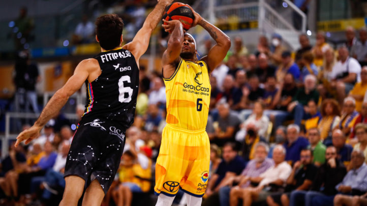 Jugador del Gran Canaria lanzando a canasta mientras es defendido por un oponente.