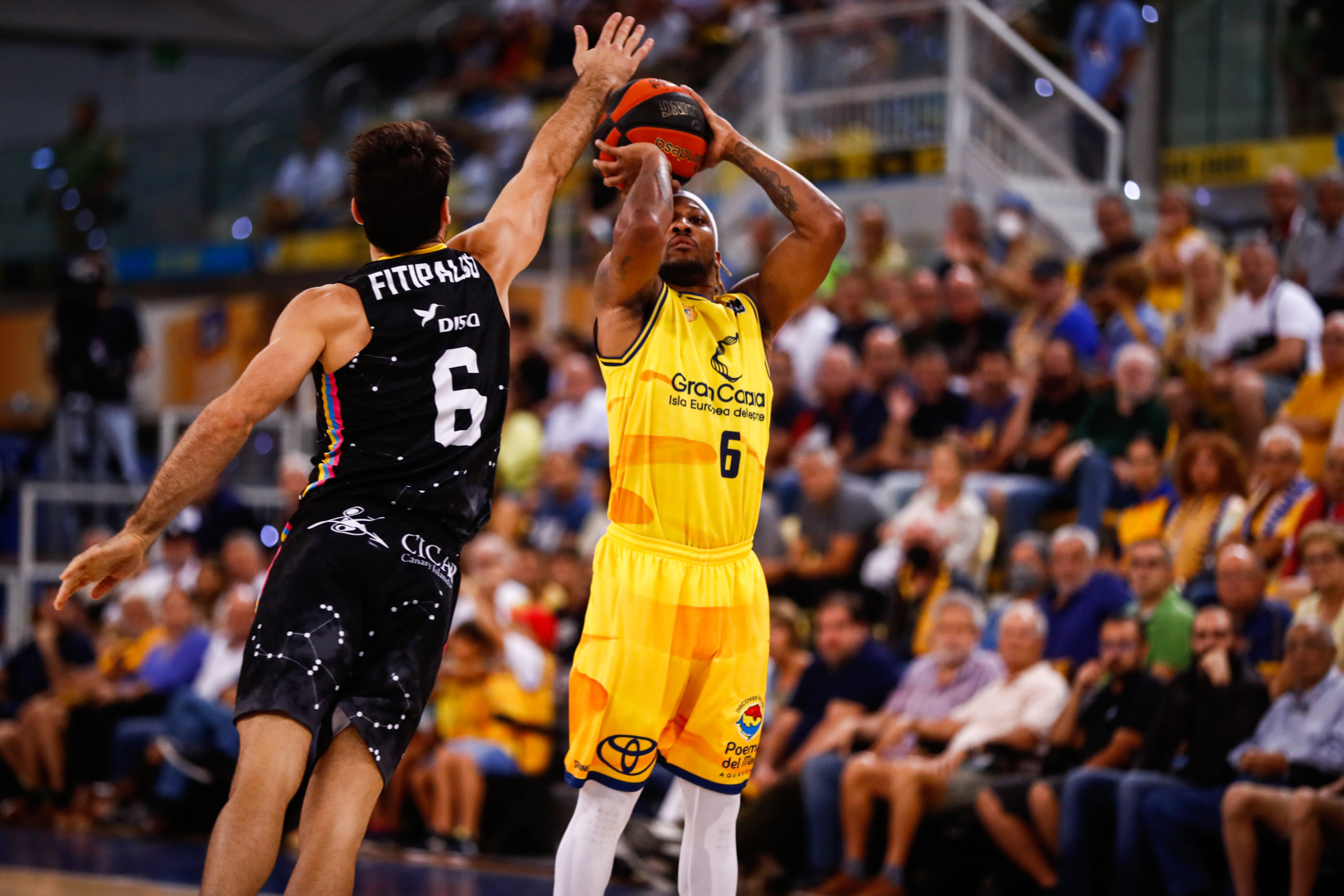 Jugador del Gran Canaria lanzando a canasta mientras es defendido por un oponente.