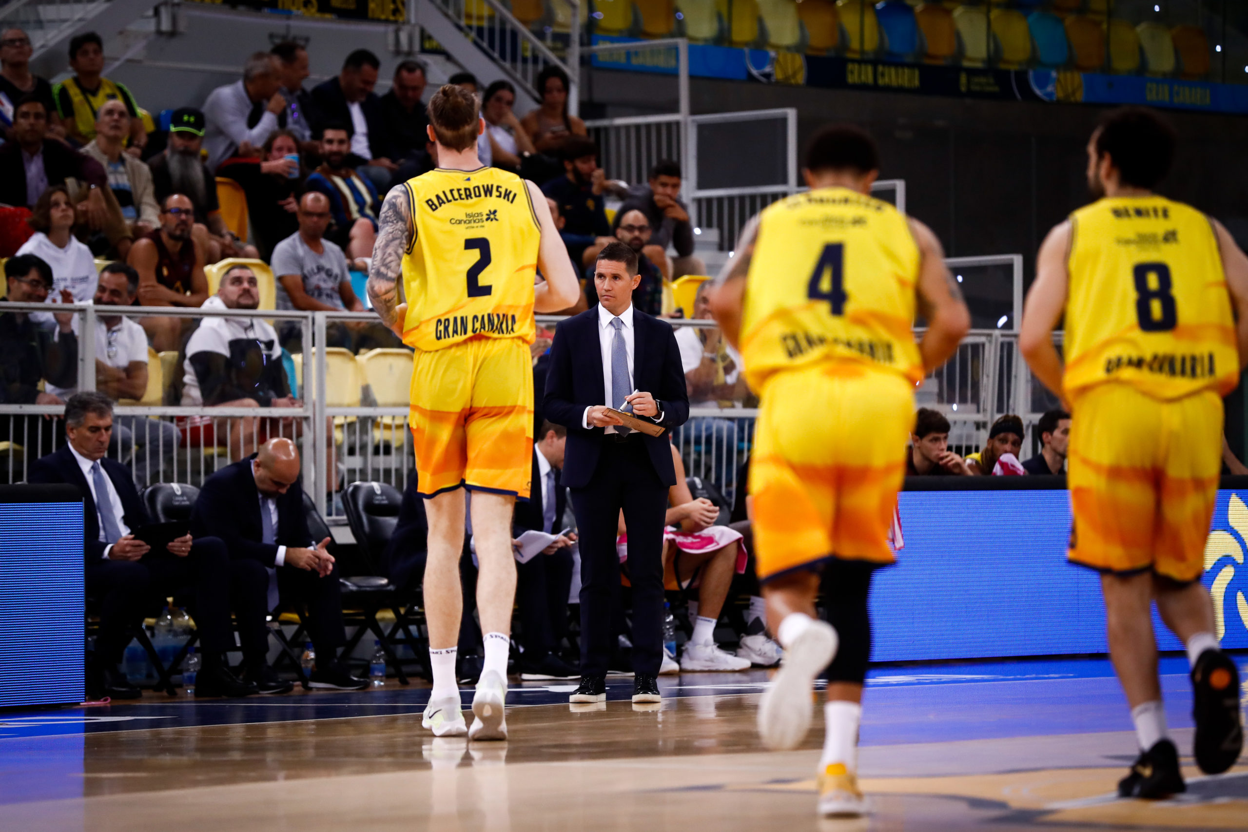 Jugadores del Gran Canaria en un partido, con un entrenador dando instrucciones.