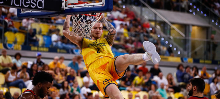Jugador del Gran Canaria encesta con un mate frente a oponentes en un partido de baloncesto.