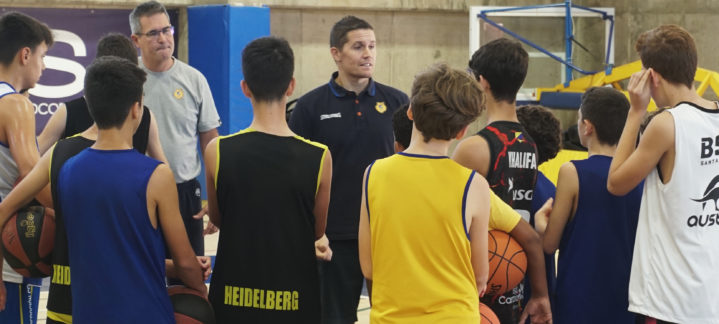 Entrenador impartiendo instrucciones a jóvenes aspirantes en clínic de baloncesto.
