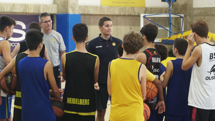 Entrenador impartiendo instrucciones a jóvenes aspirantes en clínic de baloncesto.