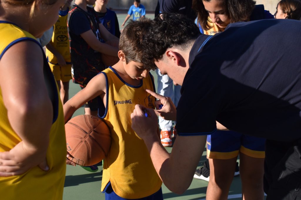 Niño con balón de baloncesto recibiendo una autógrafo mientras otros observan.