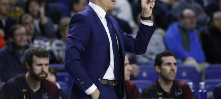 Entrenador gesticulando durante un partido, con público en el fondo.