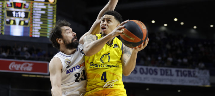 Jugador del Gran Canaria intenta anotar mientras es defendido por un rival del Madrid.