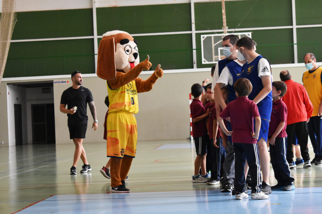 Personaje disfrazado de perro interactúa con jóvenes en un evento de baloncesto inclusivo.
