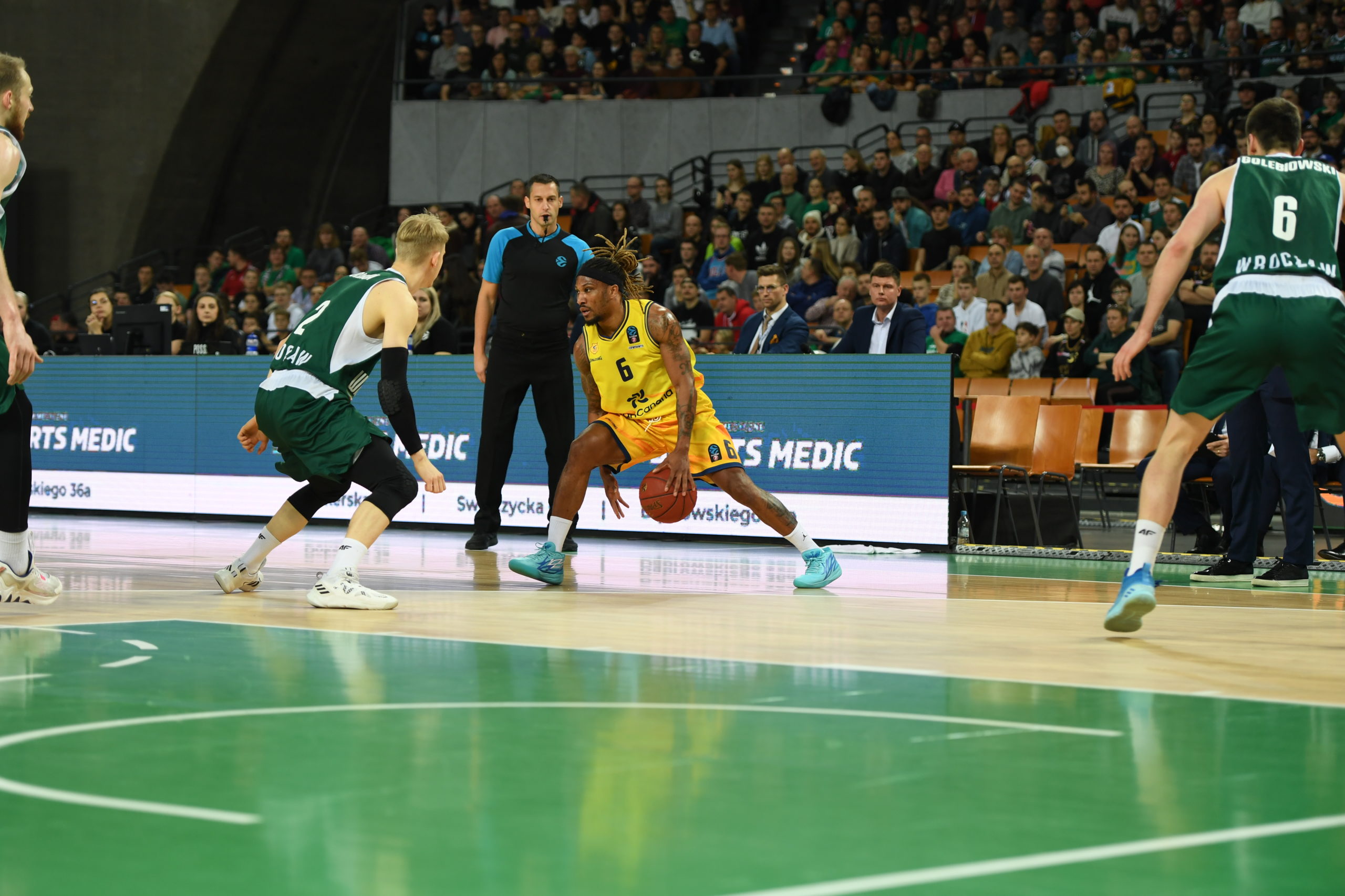 Jugador del Gran Canaria driblando ante dos oponentes del Slask Wroclaw en un partido.