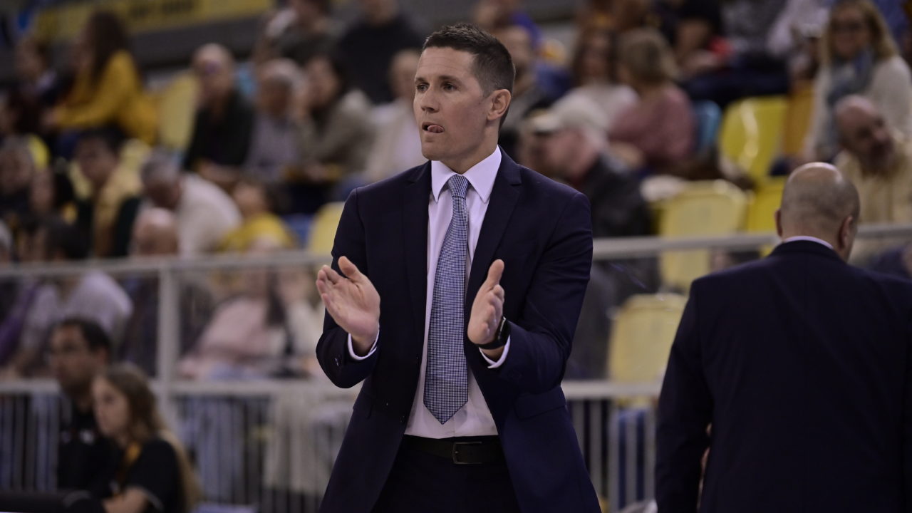 Entrenador aplaudiendo y agradeciendo a la afición durante un partido de baloncesto.