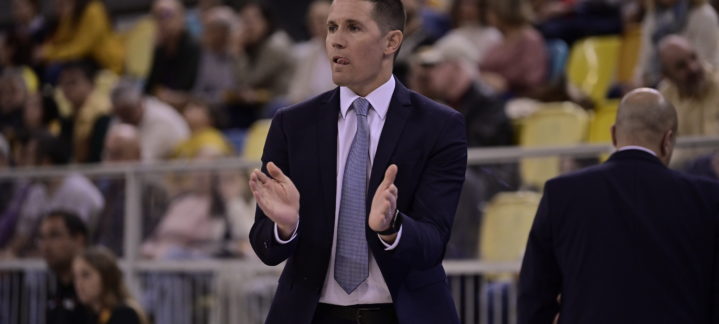 Entrenador aplaudiendo y agradeciendo a la afición durante un partido de baloncesto.