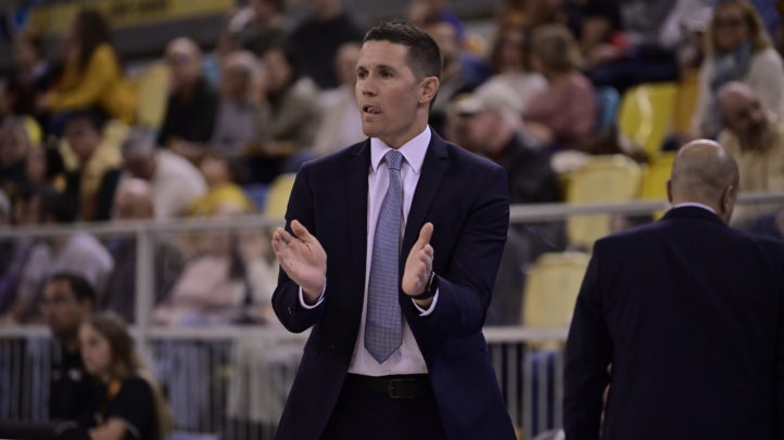 Entrenador aplaudiendo y agradeciendo a la afición durante un partido de baloncesto.
