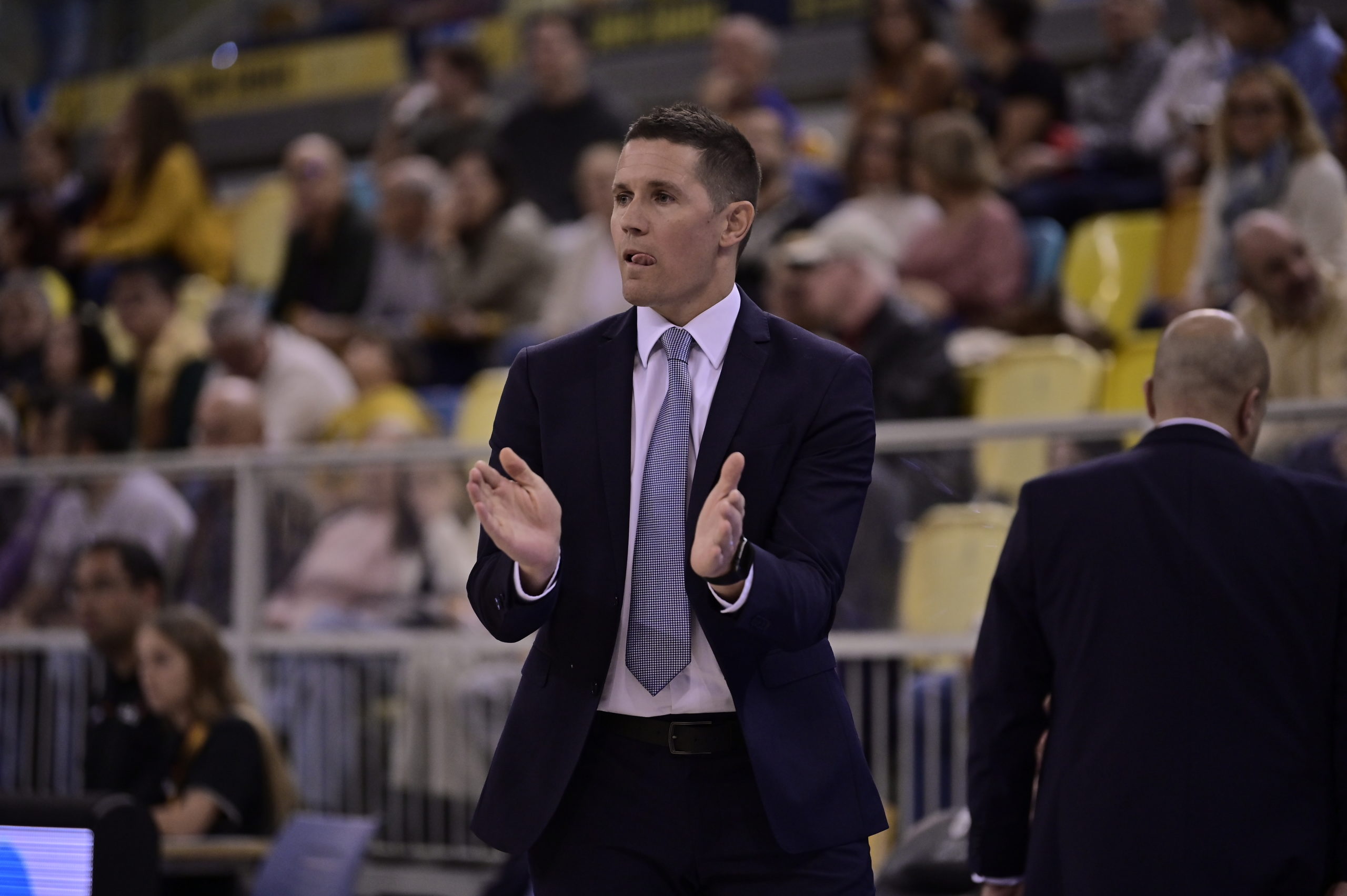 Entrenador aplaudiendo y agradeciendo a la afición durante un partido de baloncesto.