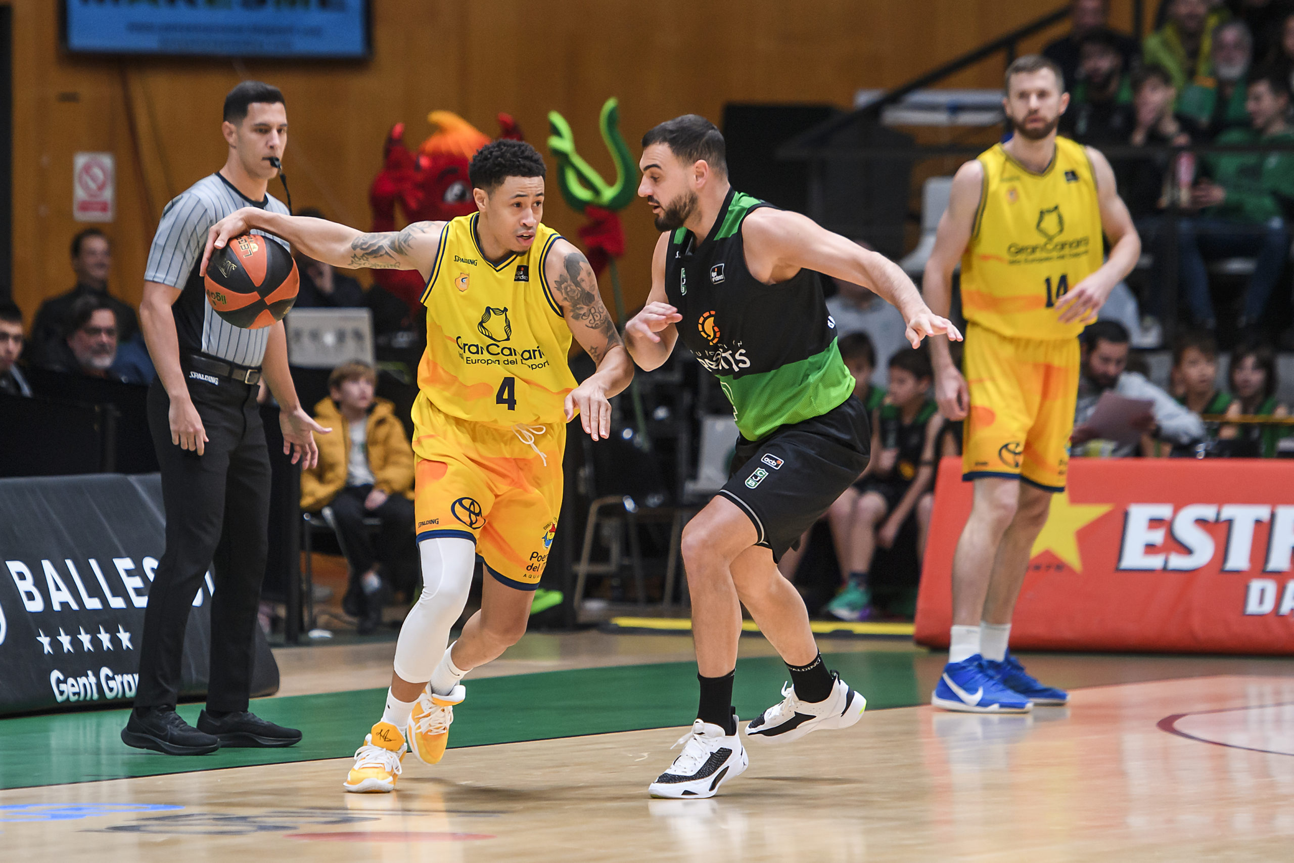 Jugadores de baloncesto en acción durante un partido, el equipo amarillo controla el balón.