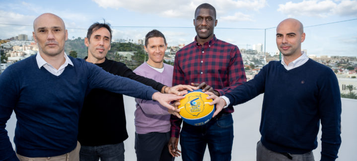 Cinco hombres participan en un desayuno informativo, sosteniendo un balón de baloncesto.