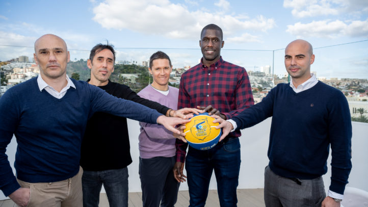 Cinco hombres participan en un desayuno informativo, sosteniendo un balón de baloncesto.