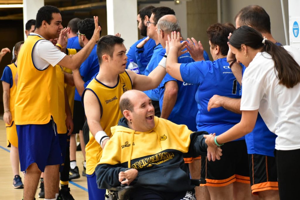 Grupo de personas interactuando y celebrando durante una jornada de baloncesto inclusivo.