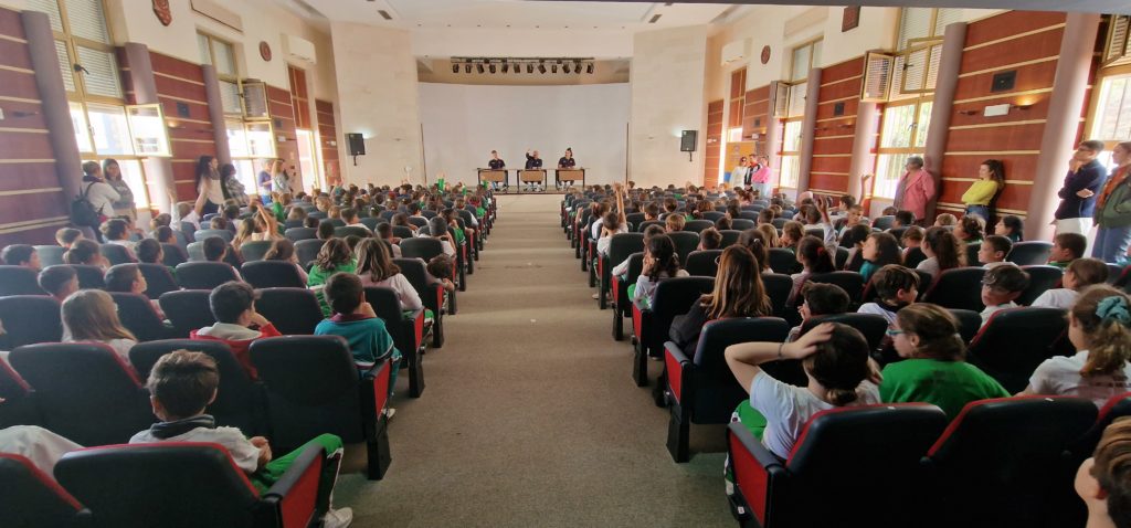 Estudiantes del CEIP Giner de los Ríos dan la bienvenida al CB Gran Canaria en un auditorio.