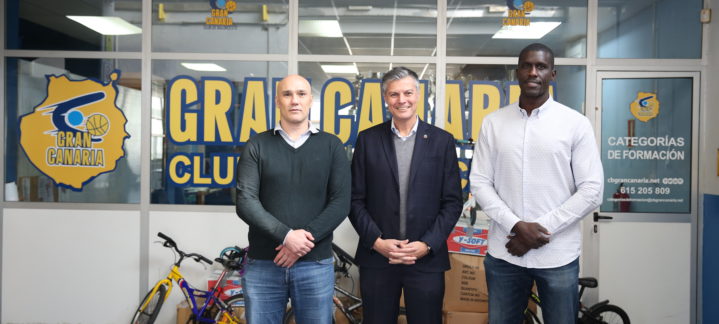 Tres personas posan frente a la sede del Club Baloncesto Gran Canaria con bicicletas de fondo.