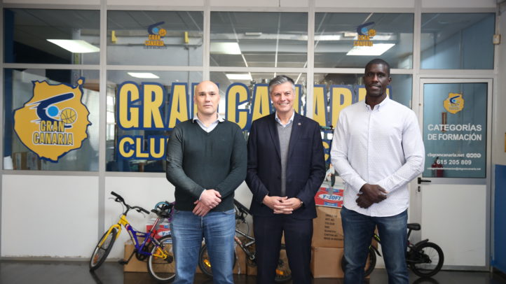 Tres personas posan frente a la sede del Club Baloncesto Gran Canaria con bicicletas de fondo.