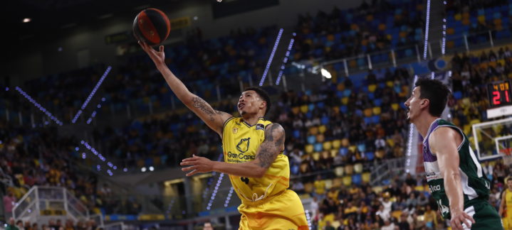 Jugador del Gran Canaria lanza a canasta mientras un rival de Unicaja lo defiende.