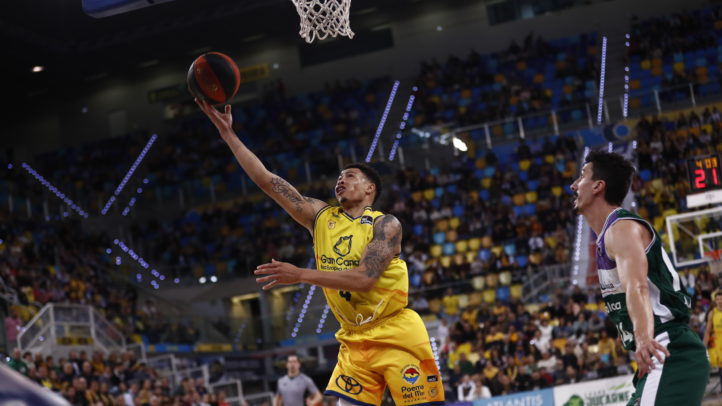 Jugador del Gran Canaria lanza a canasta mientras un rival de Unicaja lo defiende.