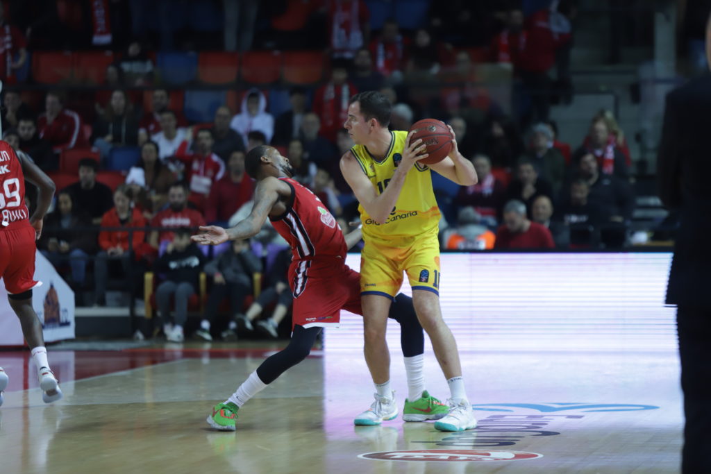 Jugador con balón en acción durante un partido de baloncesto, defendido por otro jugador.