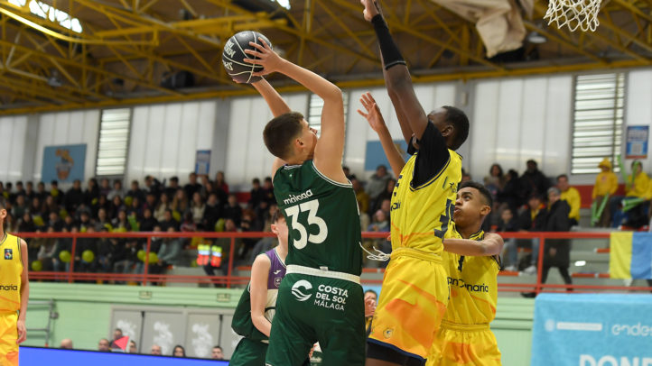 Jugador en acción lanzando el balón a canasta durante un partido de baloncesto.