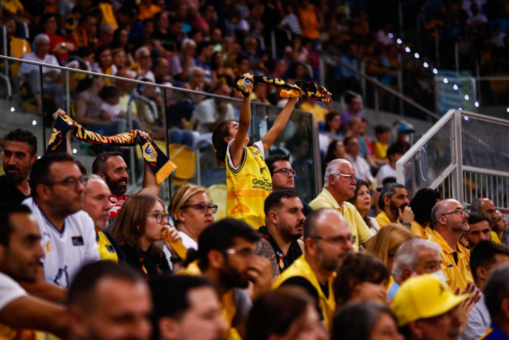 Afición animando en las gradas, con bufandas del equipo y un ambiente festivo.