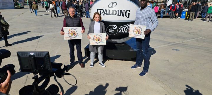 Tres personas sostienen carteles frente a una gran pelota de baloncesto en un evento.