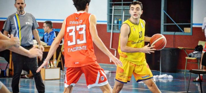 Jugadores en un partido de baloncesto, uno con balón, otro defendiendo.