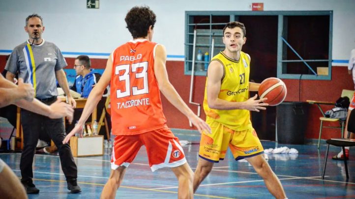 Jugadores en un partido de baloncesto, uno con balón, otro defendiendo.
