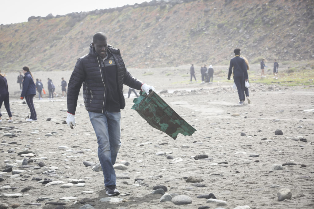 Persona recogiendo basura en la playa de Bocabarranco con grupo de voluntarios.