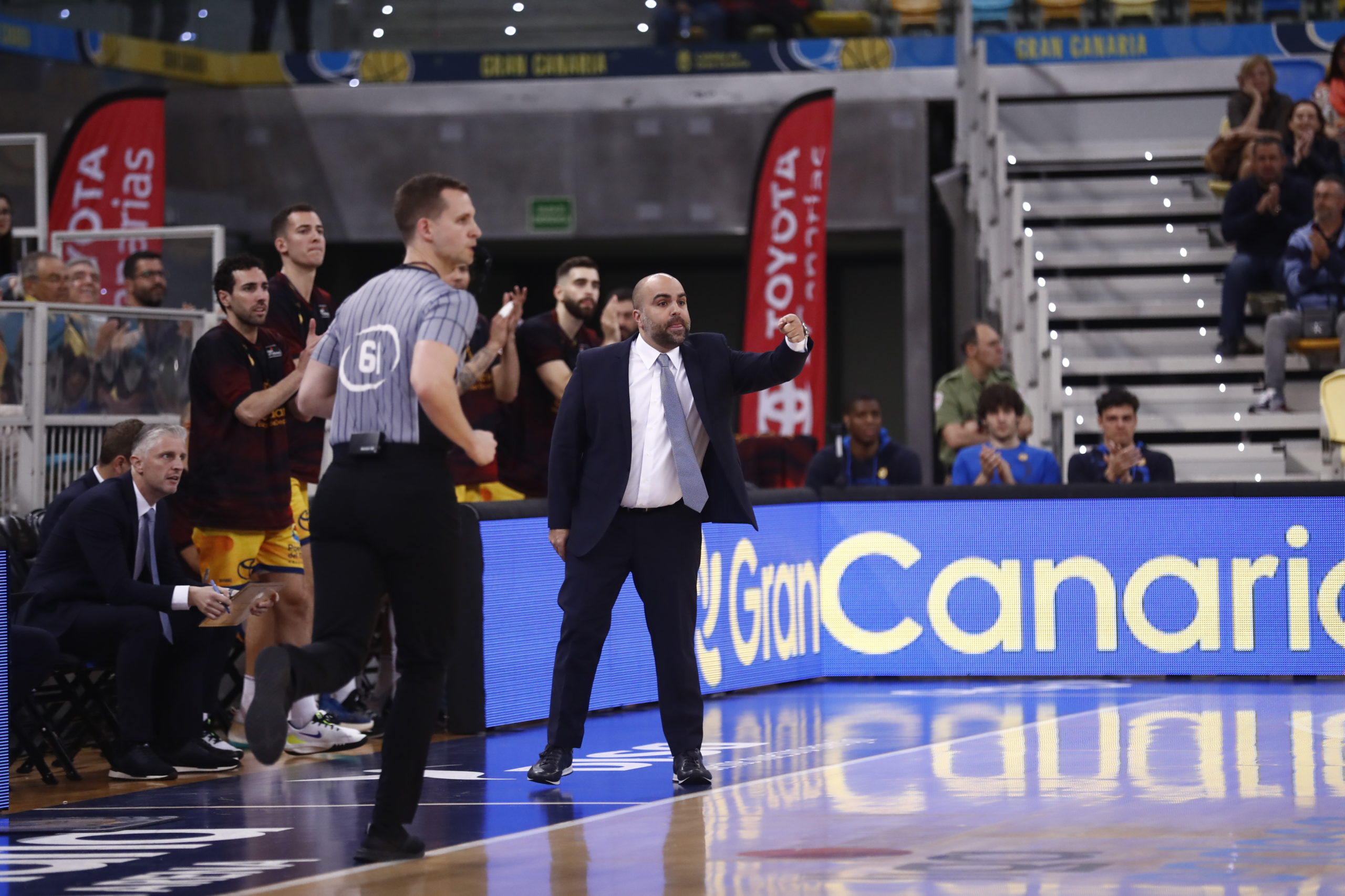 Entrenador dirigiendo al equipo durante un partido, con jugadores en el banquillo.