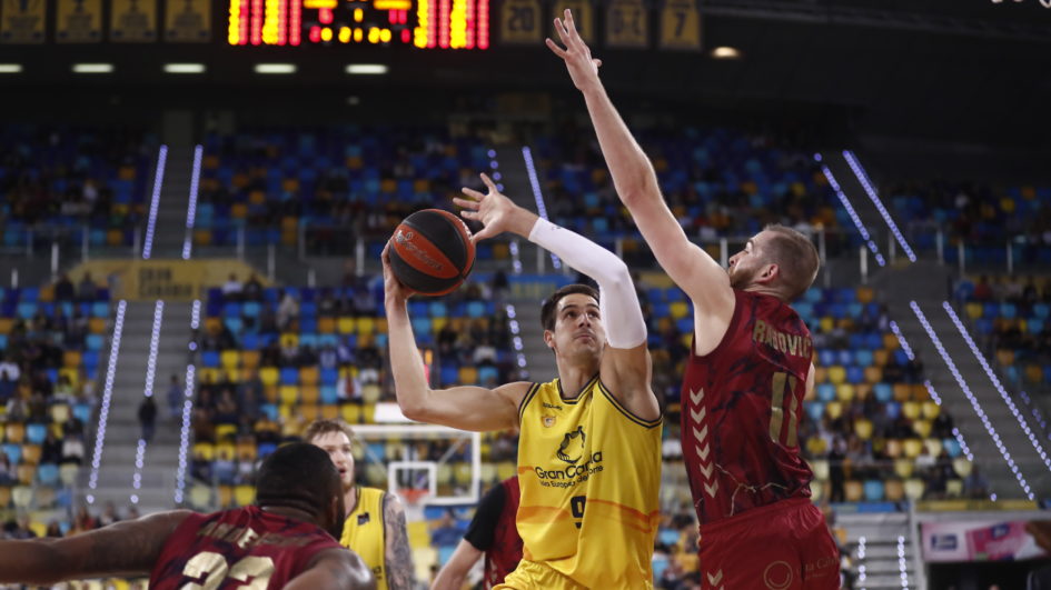 Jugador del Gran Canaria lanzando a canasta mientras es defendido por un jugador del UCAM Murcia.