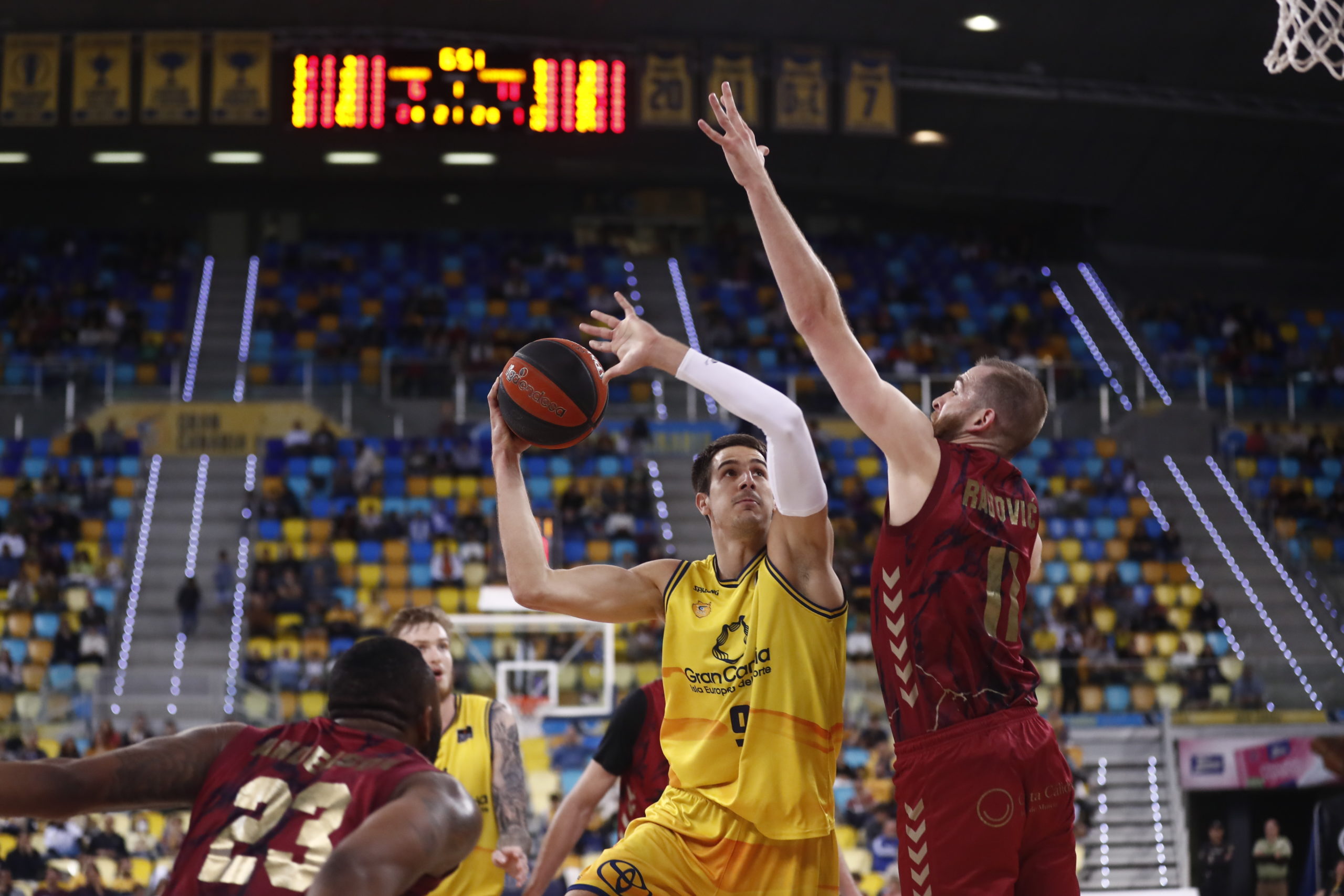 Jugador del Gran Canaria lanzando a canasta mientras es defendido por un jugador del UCAM Murcia.