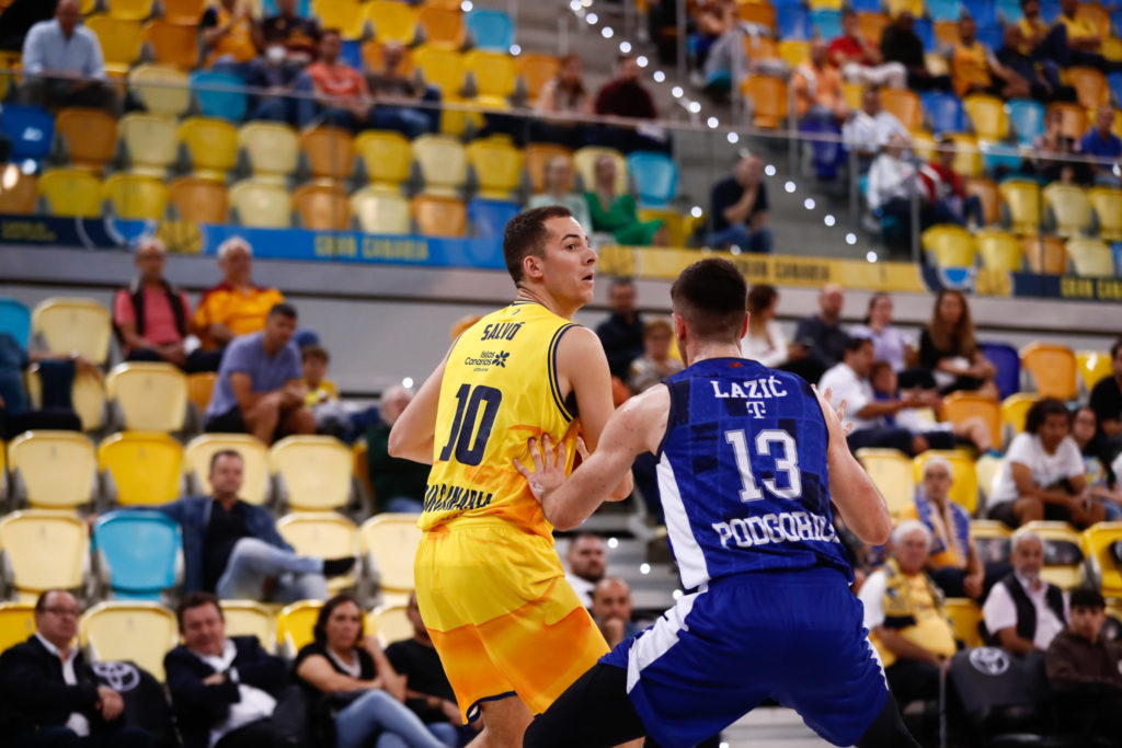 Jugadores de baloncesto en acción, con afición en las gradas del estadio.