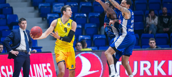 Jugadores de baloncesto en acción durante un partido, uno lanzando y otros defendiendo.