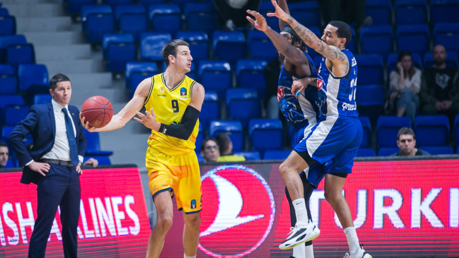 Jugadores de baloncesto en acción durante un partido, uno lanzando y otros defendiendo.
