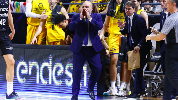 Entrenador gesticulando en un partido, rodeado de jugadores y asistentes del equipo.