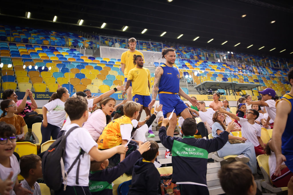 Niños y niñas interactúan con jugadores en el Gran Canaria Arena.