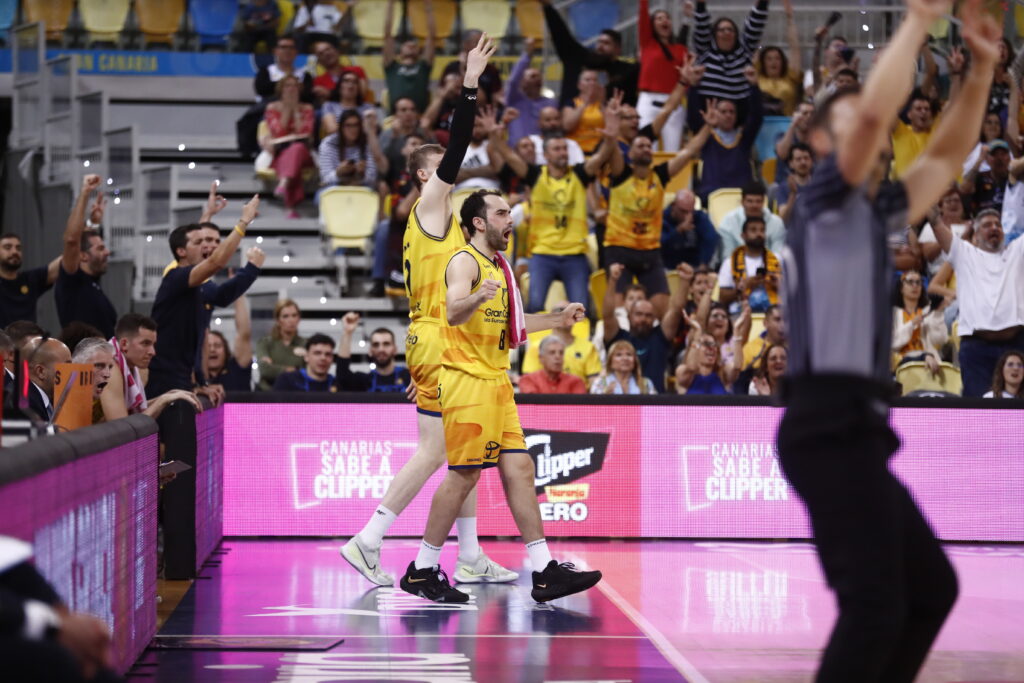 Jugadores del Gran Canaria celebran una victoria en un ambiente animado con aficionados emocionados.