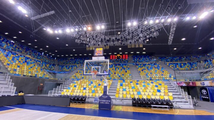 Vista del interior del pabellón con asientos vacíos y canasta de baloncesto.