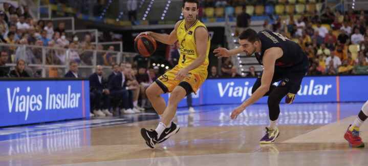 Jugador del Gran Canaria driblando el balón mientras un defensor se lanza al suelo.