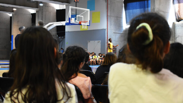 Niños y niñas atentos a la charla de un entrenador en una cancha de baloncesto.