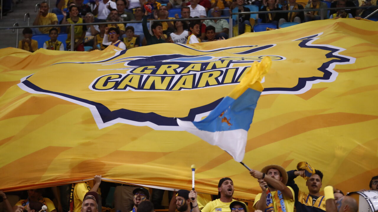 Aficionados del Club Baloncesto Gran Canaria sosteniendo una gran bandera amarilla.