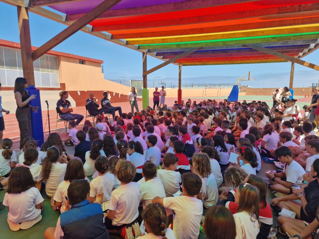 Gran grupo de niños sentados escuchando a entrenadores en un evento al aire libre.