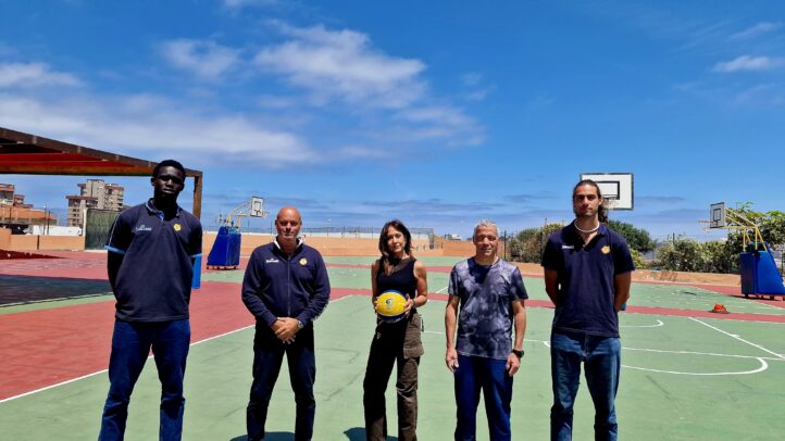 Cuatro personas posan en una cancha de baloncesto bajo un cielo despejado.