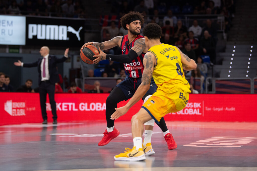 Jugador de baloncesto con balón en acción, defendido por un oponente en la cancha.