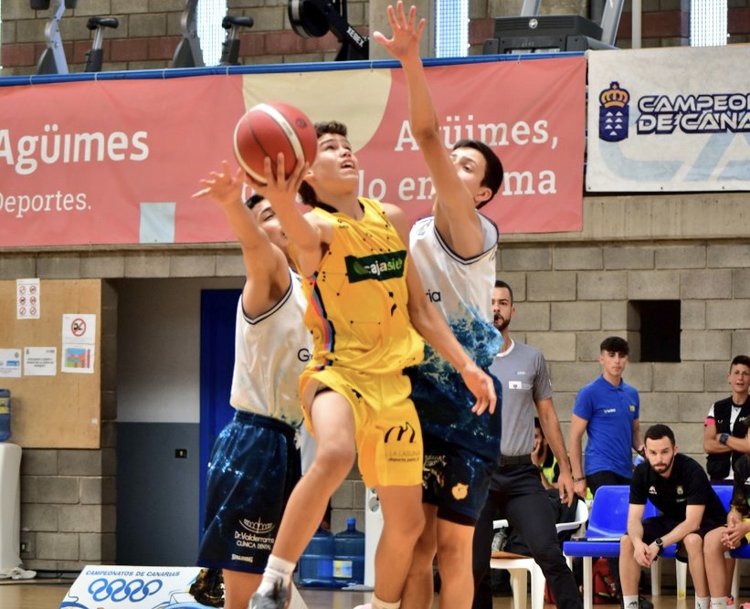 Jugador del Gran Canaria lanza a canasta ante la defensa de dos oponentes en el campeonato.
