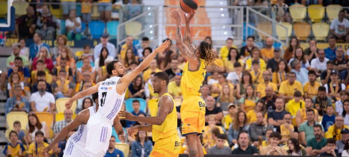 Jugador del Gran Canaria lanza el balón, mientras el rival defiende en un partido.