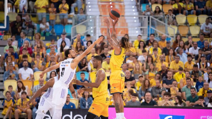 Jugador del Gran Canaria lanza el balón, mientras el rival defiende en un partido.